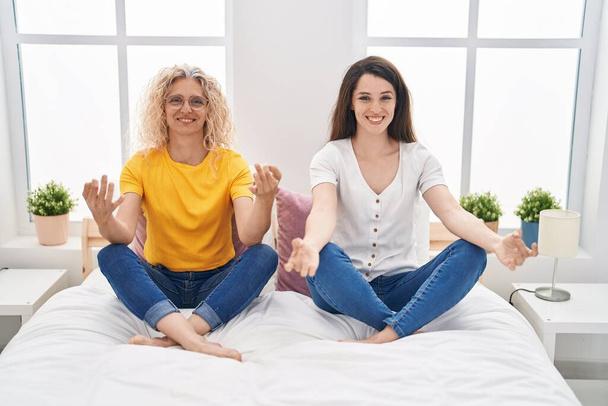 Two women mother and daughter doing yoga exercise sitting on bed at bedroom - Foto, Imagem