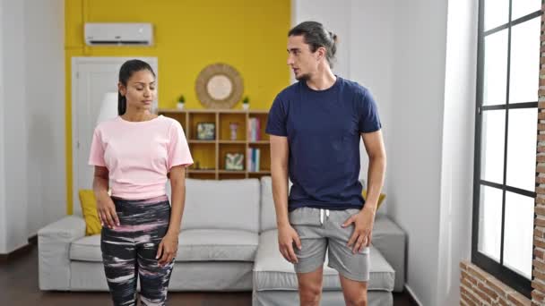 Hombre y mujer pareja sonriendo confiado entrenamiento piernas ejercicio en casa - Imágenes, Vídeo