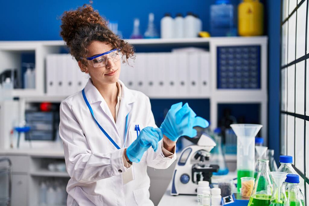 Young hispanic woman scientist wearing gloves at laboratory - Photo, Image