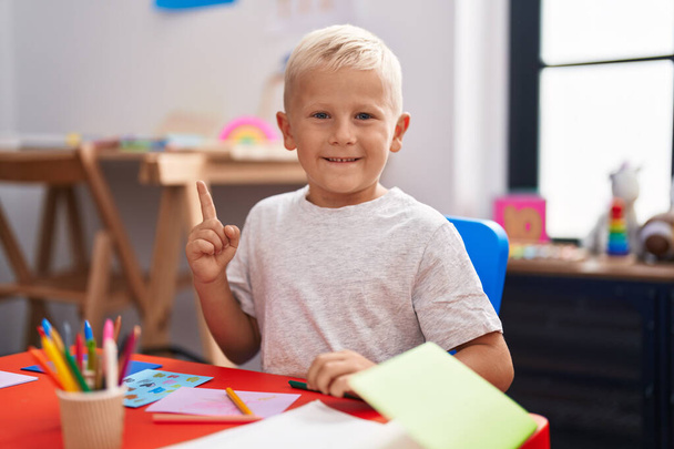 Pequeño niño caucásico pintando en la escuela sonriendo feliz señalando con la mano y el dedo a un lado  - Foto, Imagen