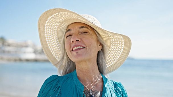 Седовласая туристка средних лет, уверенно улыбающаяся стоя на пляже - Фото, изображение