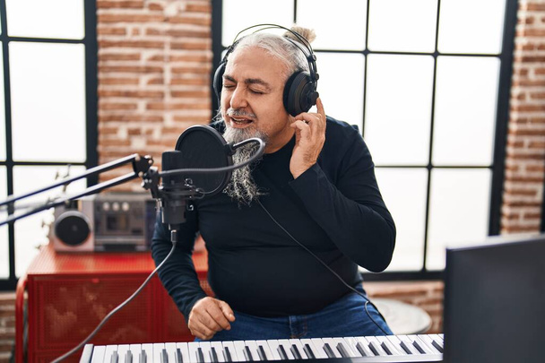 Hombre músico de pelo gris de mediana edad sonriendo confiado cantando canción en el estudio de música - Foto, Imagen