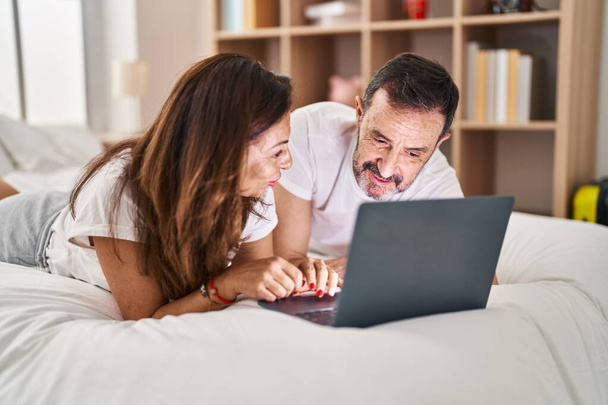 Mann und Frau mittleren Alters benutzen Laptop, der im Schlafzimmer auf dem Bett liegt - Foto, Bild