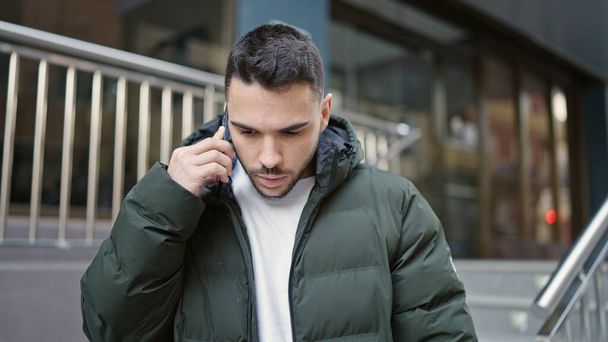 Young hispanic man talking on smartphone with serious expression at street - Foto, Bild