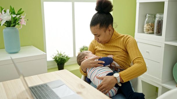 Mutter und Sohn arbeiten online, während sie ihr Baby im Esszimmer stillen - Foto, Bild