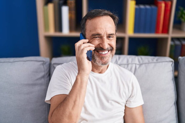 Hombre de mediana edad hablando en el teléfono inteligente sentado en el sofá en casa - Foto, imagen