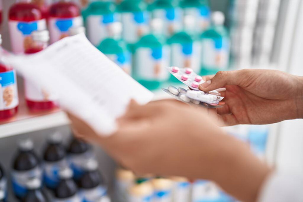 Giovane uomo biondo farmacista in possesso di pillole e carta da prescrizione in farmacia - Foto, immagini
