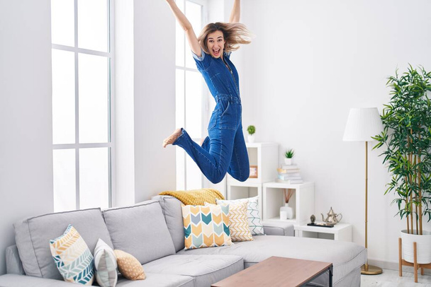 Молода жінка посміхається впевнено стрибає на дивані вдома
 - Фото, зображення