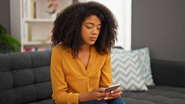 Donna afroamericana che utilizza smartphone seduto sul divano a casa - Foto, immagini