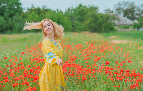 Girl in yellow with blue elements embroidered Boho dress. Fashionable blonde head lady in poppy field - Photo, Image