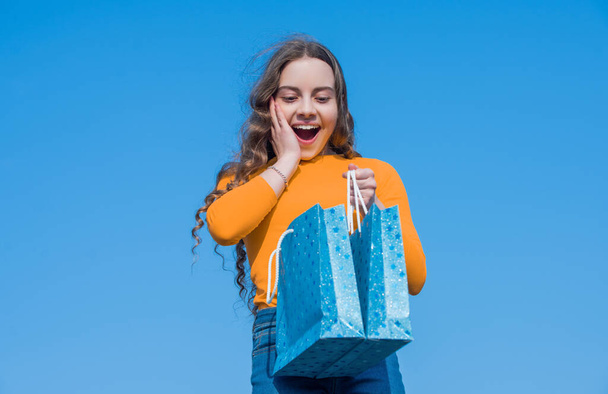 surprised teen girl opening shopping bag, blue yellow. - Фото, зображення