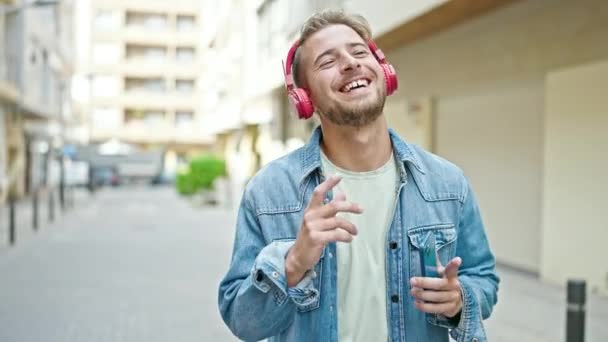 Młody biały mężczyzna słuchający muzyki i tańczący na ulicy - Materiał filmowy, wideo
