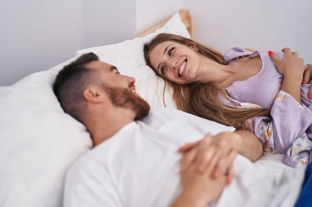 Мужчина и женщина уверенно улыбаются, лежа на кровати в спальне - Фото, изображение