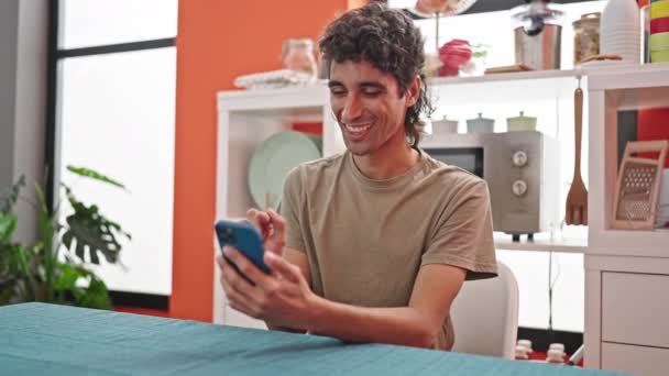 Fiatal spanyol férfi használ okostelefon ül az asztalon ebédlőben - Felvétel, videó