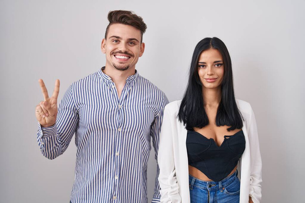 Young hispanic couple standing over white background showing and pointing up with fingers number two while smiling confident and happy.  - Photo, Image