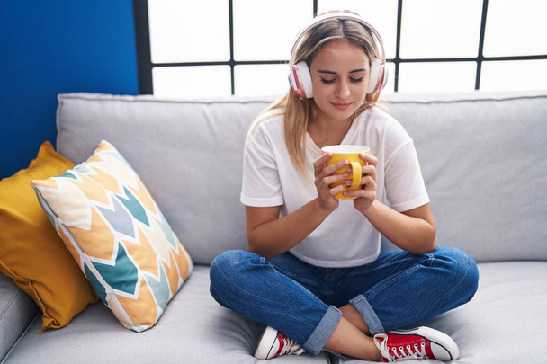 Mujer rubia joven escuchando música tomando café en casa - Foto, imagen