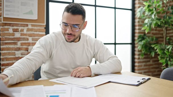 Молодий іспаномовний чоловік бізнесмен читає документ в офісі
 - Фото, зображення