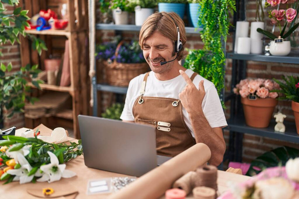 Белый мужчина с усами, работающий в цветочном магазине, делает видеозвонок, улыбаясь, показывая пальцем и рукой.  - Фото, изображение