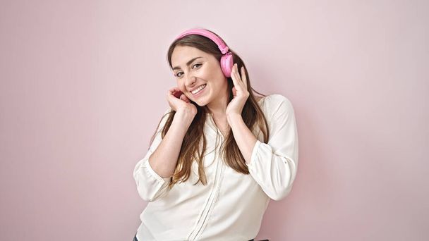 Junge schöne hispanische Frau hört Musik und tanzt vor isoliertem rosa Hintergrund - Foto, Bild