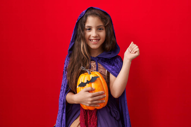 Маленькая латиноамериканка в костюме ведьмы на Хэллоуин гордится, празднует победу и успех очень взволнован с поднятыми руками  - Фото, изображение