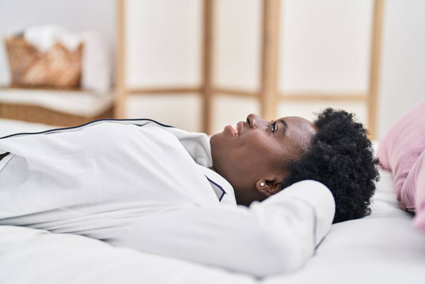 Νεαρή Αφροαμερικανή γυναίκα χαμογελά με αυτοπεποίθηση ξαπλωμένη στο κρεβάτι στο υπνοδωμάτιο - Φωτογραφία, εικόνα