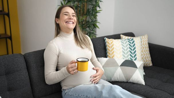 Young pregnant woman drinking coffee touching belly at home - Foto, immagini