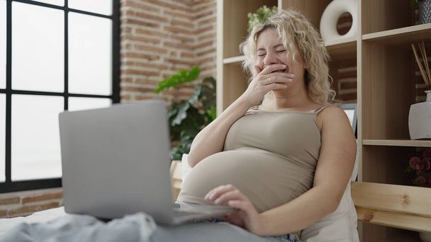 Junge schwangere Frau sieht Video auf Laptop im Schlafzimmer liegend - Foto, Bild