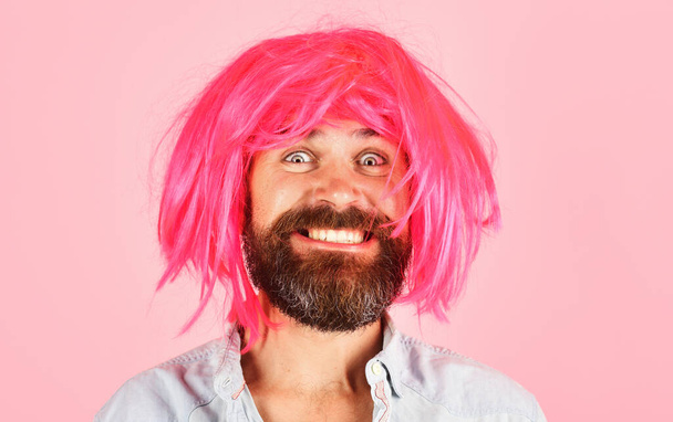 Hassu parrakas mies vaaleanpunaisessa peruukissa. Hymyilevä mies, jolla on parta ja viikset värillisessä peruukissa. Kasvojen ilme. Tunteet. Hipster on vaarassa. Juhlien aika. Tyylikäs mies värikkäillä hiuksilla. Parturimainonta - Valokuva, kuva
