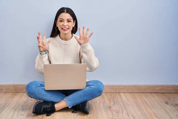 Giovane donna che utilizza il computer portatile seduto sul pavimento a casa mostrando e indicando con le dita numero nove mentre sorride fiducioso e felice.  - Foto, immagini