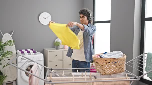 Fiatal spanyol férfi zenét hallgat, ruhákat lóg a ruhaszekrényre a mosodában. - Felvétel, videó