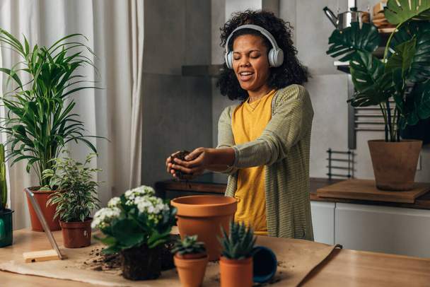 Cheerful woman listens to music while potting her plants. - Valokuva, kuva