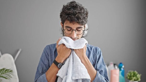 Jeune homme hispanique souriant confiant sentant serviette propre à la buanderie - Photo, image