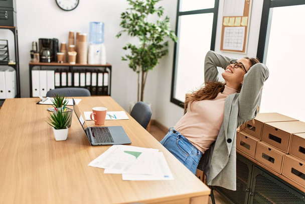 Young beautiful hispanic woman business worker relaxed with hands on head at office - Photo, Image