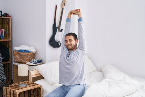 Young man waking up stretching arms at bedroom - Foto, afbeelding