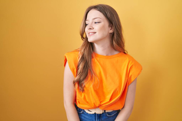 Caucasian woman standing over yellow background looking away to side with smile on face, natural expression. laughing confident.  - Foto, immagini