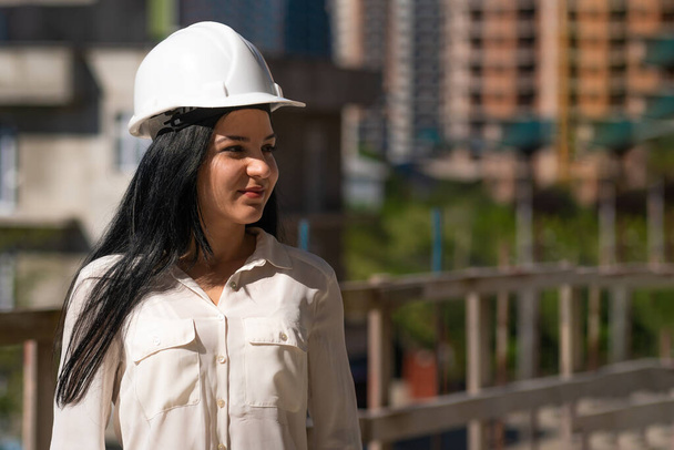 Young beautiful female engineer in a hard hat at a construction site on a sunny day looks away, copy space. - Фото, зображення
