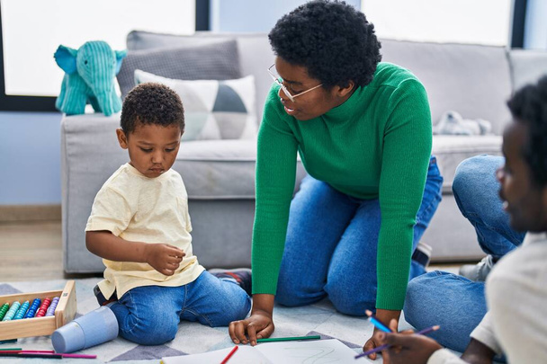 African american family drawing on notebook sitting on floor at home - Foto, afbeelding