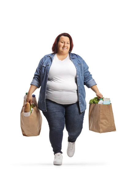 Overweight young woman carrying grocery bags and walking isolated on white background - Photo, image