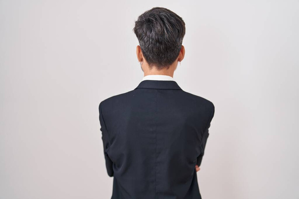 Young hispanic man with tattoos wearing business suit and tie standing backwards looking away with crossed arms  - Fotó, kép