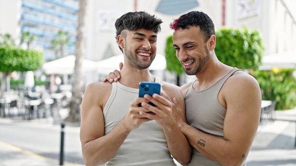 Двоє чоловіків посміхаються впевнено використовуючи смартфон на терасі кав'ярні
 - Фото, зображення