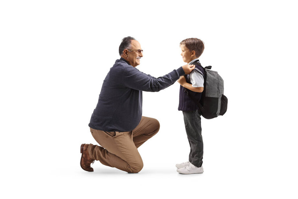 Full length profile shot of a grandfather helping a boy getting ready for school isolated on white background - Foto, imagen