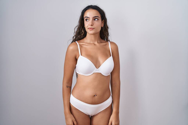 Young hispanic woman wearing white lingerie smiling looking to the side and staring away thinking.  - Foto, Imagen