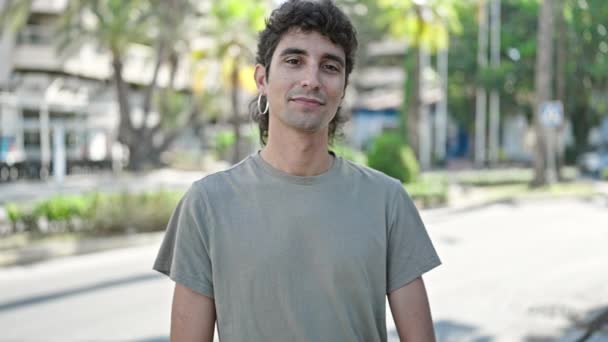 Junger hispanischer Mann lächelt zuversichtlich und macht Okay-Schild mit erhobenem Daumen auf Straße - Filmmaterial, Video