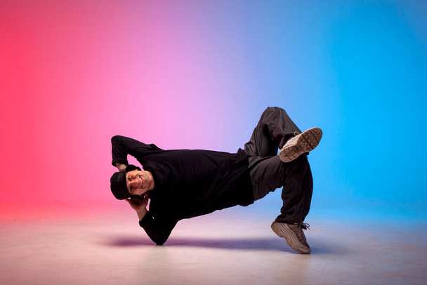 mladý kluk hiphop performer break dance v neonovém klubu osvětlení a dělá akrobatický trik, mužský tanečník stojí v akrobatické póze - Fotografie, Obrázek