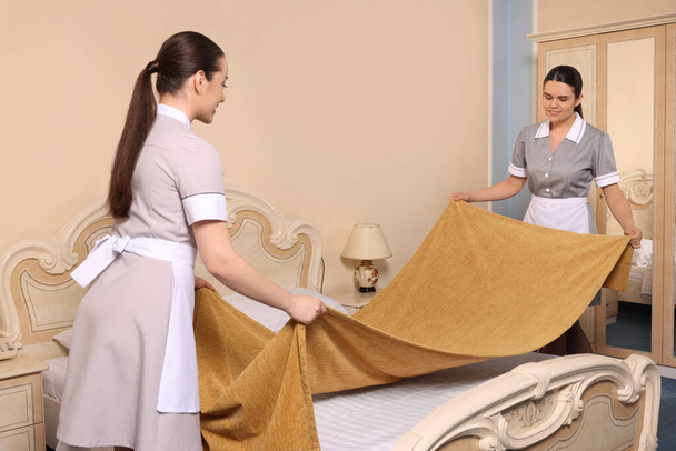 Young chambermaids making bed in hotel room - Photo, image
