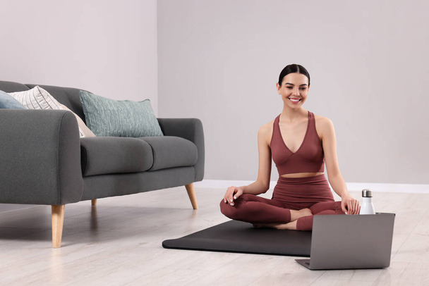 Woman in sportswear meditating near laptop at home, space for text - Фото, зображення