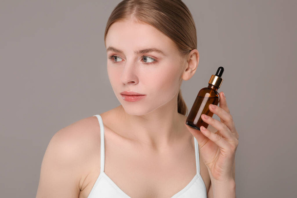 Beautiful young woman with bottle of essential oil on light grey background - Foto, Imagen