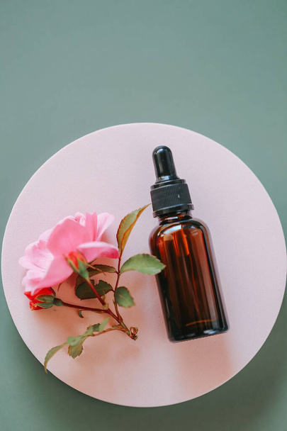  cosmetics with rose extract.Rose oil in a glass bottle on a pink podium on a gray background. View from above .Aromatherapy and cosmetics.Organic natural rose oil.Organic bio cosmetics - Zdjęcie, obraz