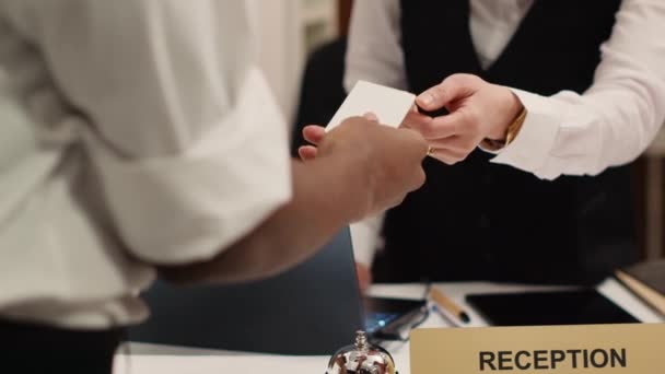 Close up of receptionist handing card key to african american tourist during check in process. Business travelling guest ready to enjoy hotel stay after receiving room access - Footage, Video