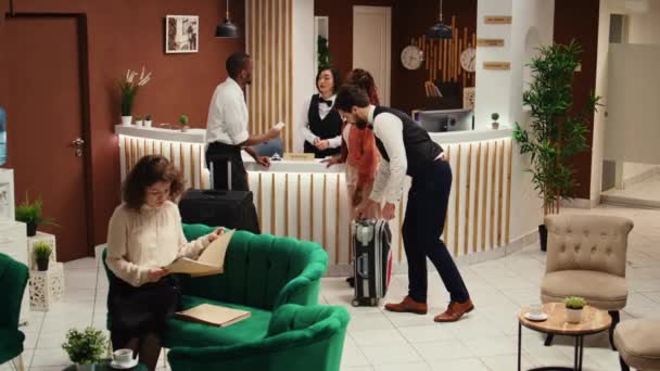 Koncentrált hotel menedzser ellenőrzi turisták foglalás papírmunka közben segítik a concierge személyzet. Bellboy segít a vendégek poggyász után check-in folyamat vége. - Felvétel, videó